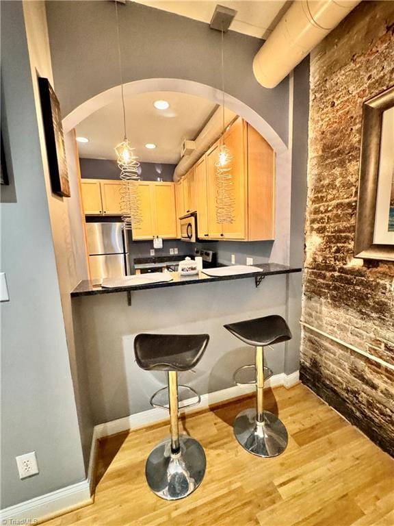220 Market St Unit 110, Greensboro, NC 27401 - kitchen featuring appliances with stainless steel finishes, brick wall, light brown cabinets, wood finished floors, and arched walkways