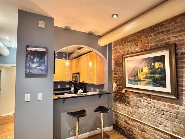 220 Market St Unit 110, Greensboro, NC 27401 - kitchen with stainless steel microwave, electric stove, a breakfast bar area, wood finished floors, and brick wall