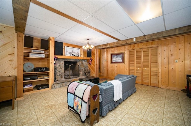 interior space with a paneled ceiling, light tile floors, a chandelier, wooden walls, and a stone fireplace