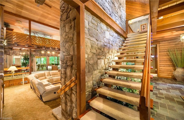 stairway with wooden ceiling, rustic walls, ceiling fan, and a towering ceiling