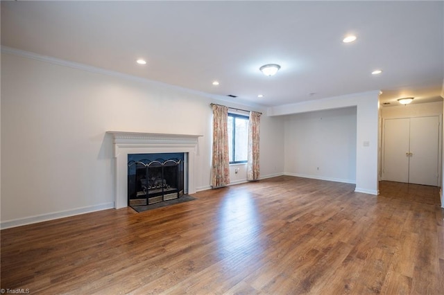 unfurnished living room featuring crown molding, recessed lighting, a fireplace with flush hearth, wood finished floors, and baseboards