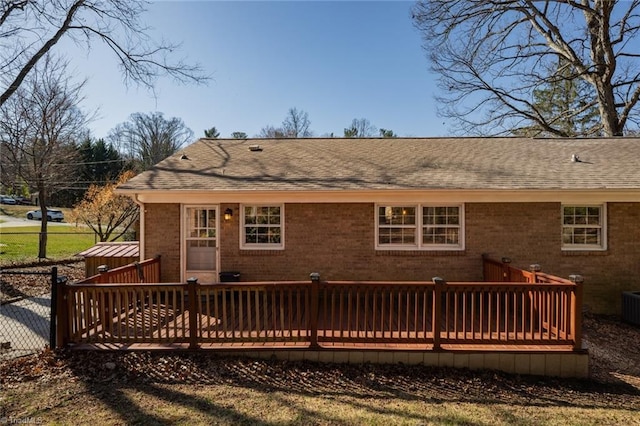 back of property featuring brick siding, a wooden deck, and roof with shingles