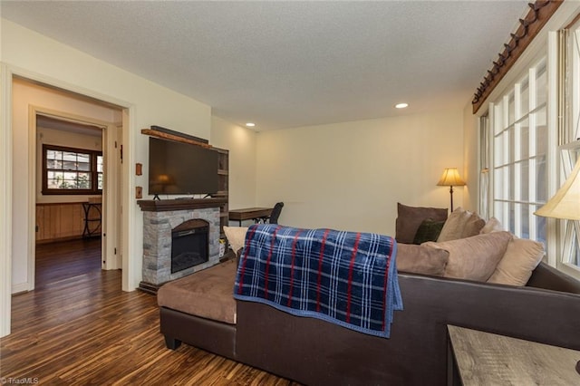 living area featuring recessed lighting, a textured ceiling, a stone fireplace, and dark wood finished floors