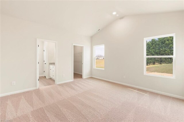 unfurnished bedroom with baseboards, vaulted ceiling, a walk in closet, and light carpet