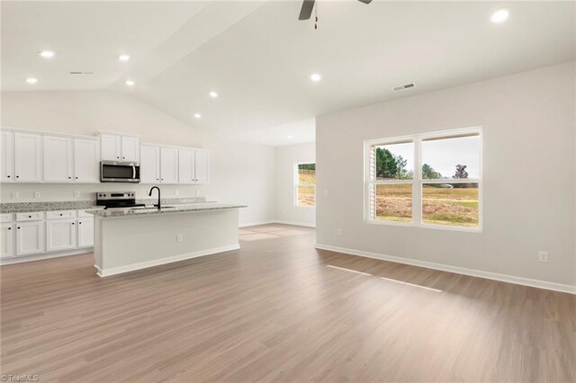 kitchen with an island with sink, a sink, light wood finished floors, appliances with stainless steel finishes, and visible vents