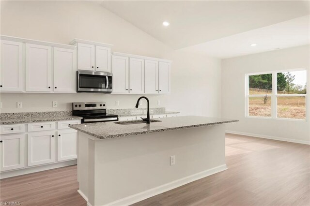 kitchen featuring white cabinetry, lofted ceiling, stainless steel appliances, a sink, and light stone counters