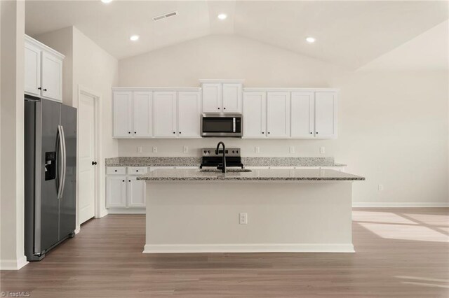 kitchen with light wood-type flooring, stainless steel appliances, an island with sink, white cabinets, and light stone countertops