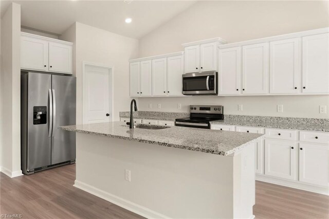 kitchen featuring lofted ceiling, a center island with sink, a sink, white cabinets, and appliances with stainless steel finishes