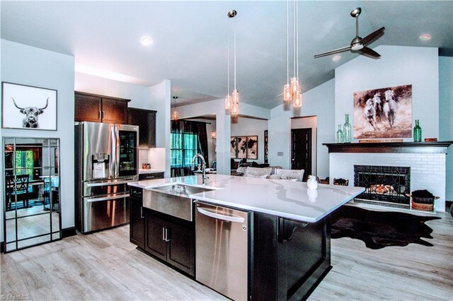 kitchen featuring pendant lighting, dishwasher, an island with sink, light hardwood / wood-style floors, and vaulted ceiling