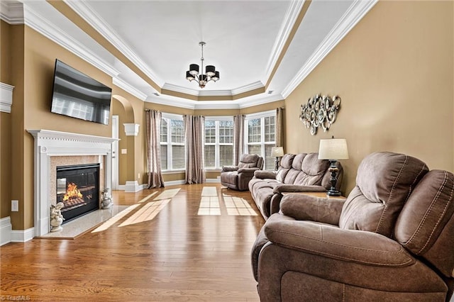 living area featuring a tray ceiling, a premium fireplace, ornamental molding, a chandelier, and light wood-type flooring