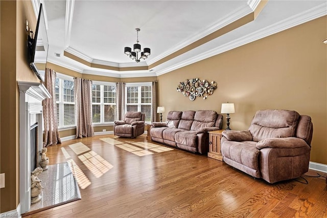 living room with light wood-type flooring, a tray ceiling, a notable chandelier, and a high end fireplace