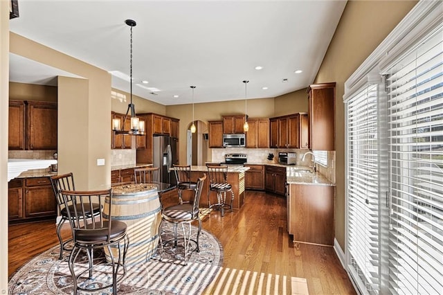 kitchen with a center island, brown cabinets, dark wood finished floors, stainless steel appliances, and hanging light fixtures