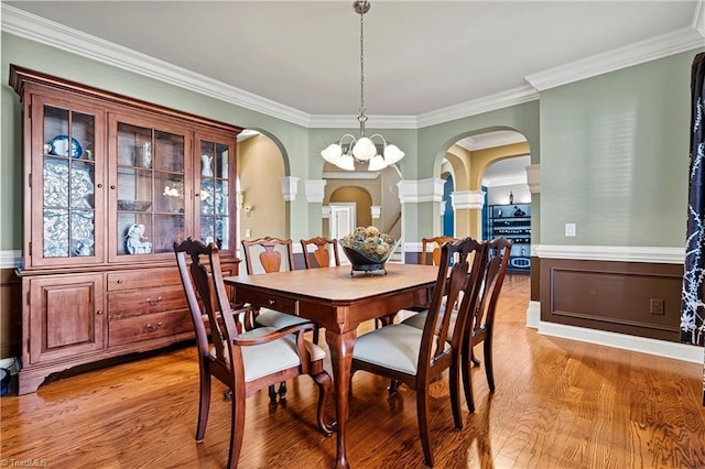 dining room featuring arched walkways, ornamental molding, and light wood-style floors