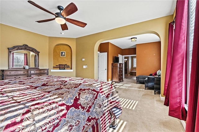 bedroom with light carpet, ceiling fan, and arched walkways