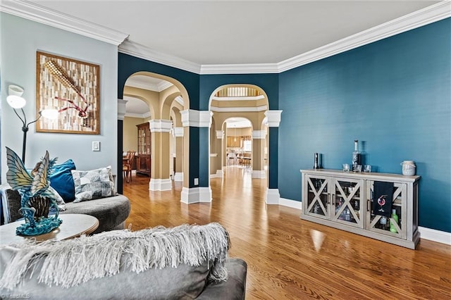 interior space featuring decorative columns, baseboards, arched walkways, ornamental molding, and wood finished floors