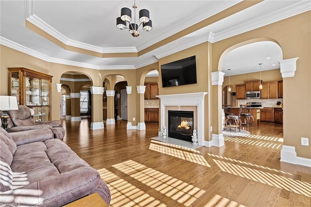 living room with baseboards, a raised ceiling, wood finished floors, a notable chandelier, and a multi sided fireplace