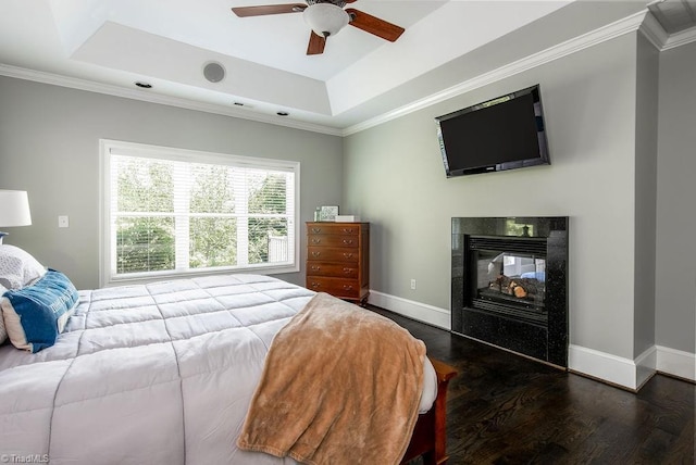 bedroom with a fireplace, wood finished floors, a raised ceiling, baseboards, and ornamental molding