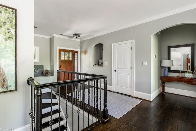 hallway featuring ornamental molding, wood finished floors, baseboards, arched walkways, and an upstairs landing