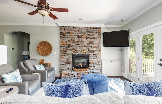 living room with crown molding, visible vents, wood finished floors, a stone fireplace, and ceiling fan