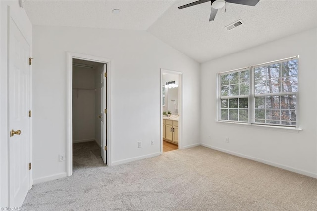 unfurnished bedroom featuring lofted ceiling, a textured ceiling, light colored carpet, visible vents, and a spacious closet