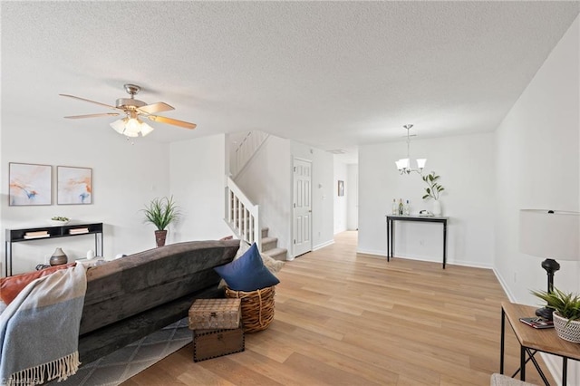 living room featuring baseboards, stairs, a textured ceiling, light wood-type flooring, and ceiling fan with notable chandelier