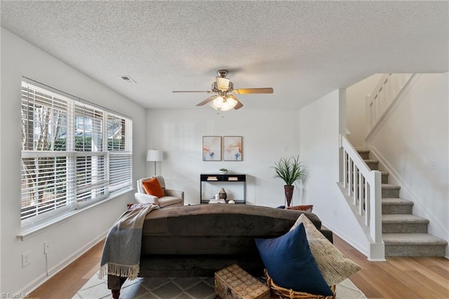 living area with stairs, a textured ceiling, wood finished floors, and baseboards