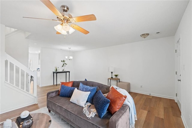 living room with ceiling fan with notable chandelier, stairway, wood finished floors, and baseboards