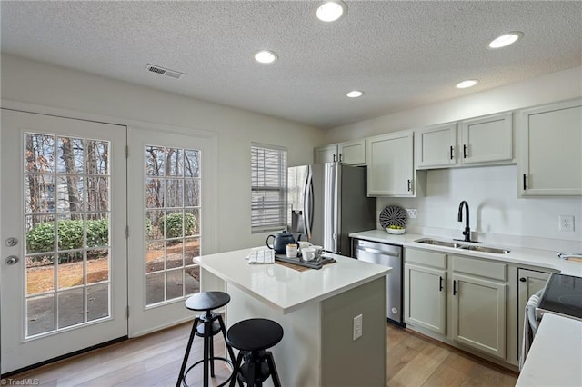 kitchen with a breakfast bar area, stainless steel appliances, a kitchen island, a sink, and light wood-type flooring