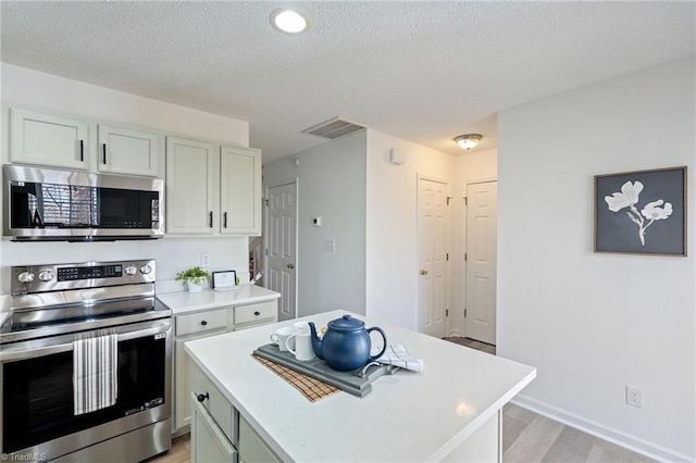 kitchen with light wood-style flooring, visible vents, light countertops, appliances with stainless steel finishes, and a center island