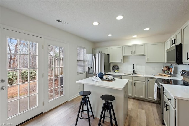 kitchen with a center island, light wood finished floors, visible vents, appliances with stainless steel finishes, and a sink