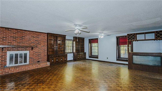 unfurnished living room featuring ceiling fan, a textured ceiling, dark parquet floors, and a fireplace