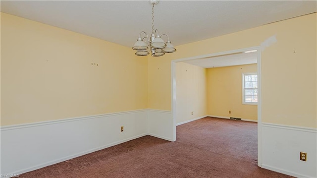 carpeted empty room featuring an inviting chandelier