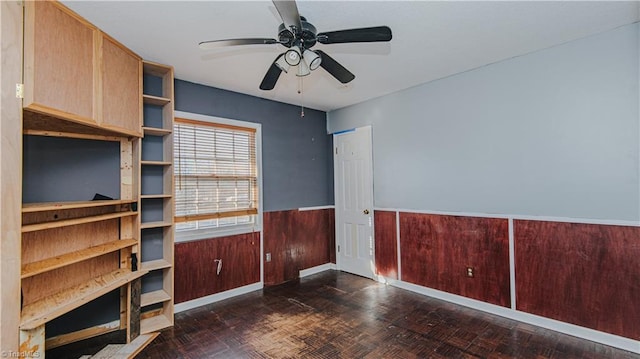 unfurnished office with ceiling fan, dark parquet flooring, and wooden walls