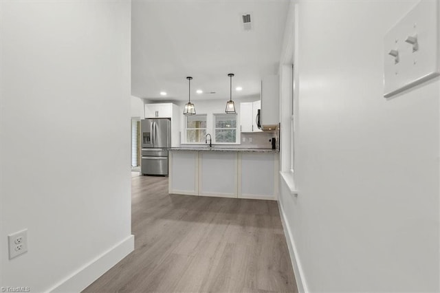 kitchen with baseboards, a peninsula, light wood-style flooring, white cabinetry, and stainless steel fridge