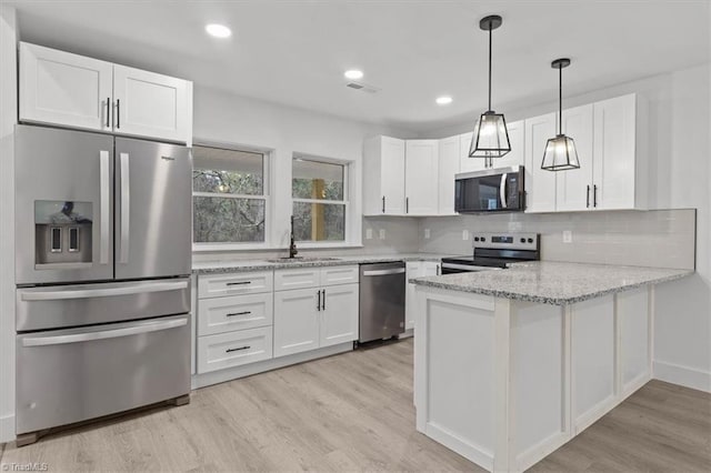 kitchen with light stone countertops, a peninsula, a sink, stainless steel appliances, and white cabinetry