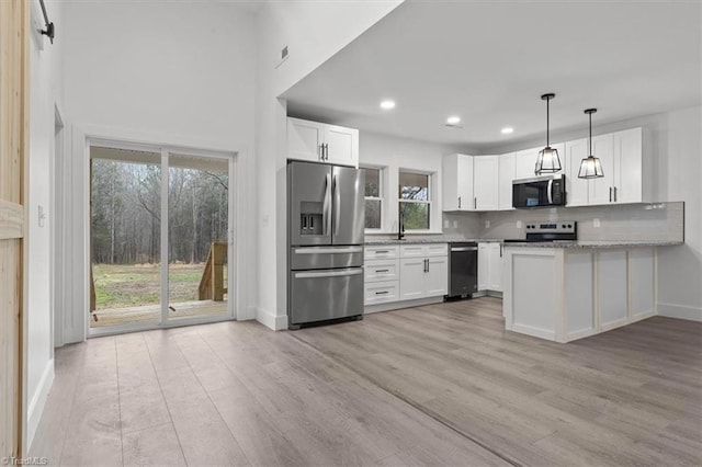 kitchen with light wood finished floors, pendant lighting, decorative backsplash, appliances with stainless steel finishes, and white cabinets