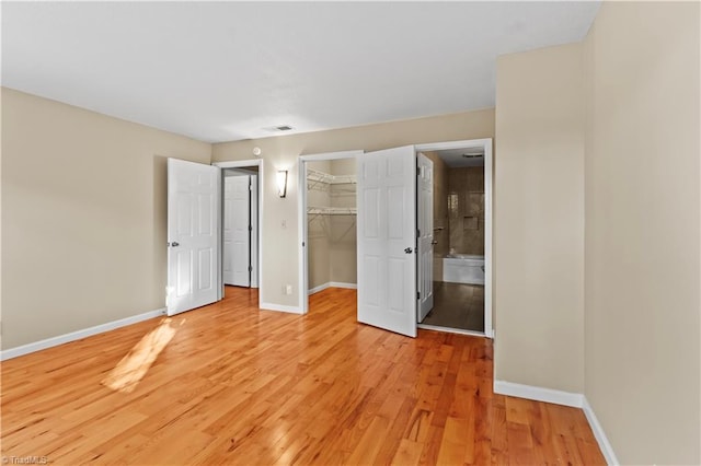 unfurnished bedroom featuring a closet, ensuite bathroom, light hardwood / wood-style floors, and a walk in closet