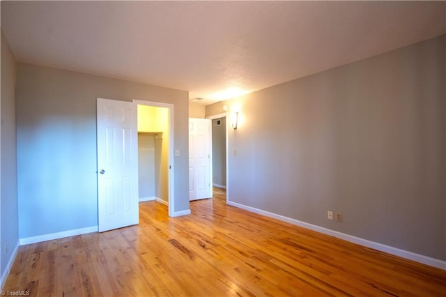 unfurnished bedroom with a spacious closet, a closet, and light wood-type flooring