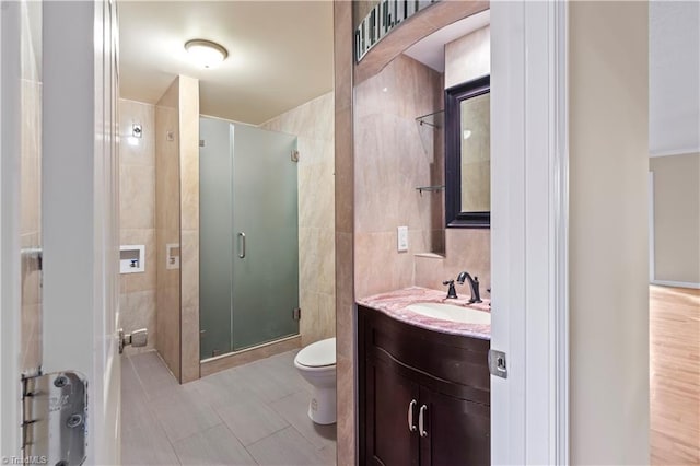 bathroom featuring tile flooring, a shower with shower door, tile walls, vanity, and toilet