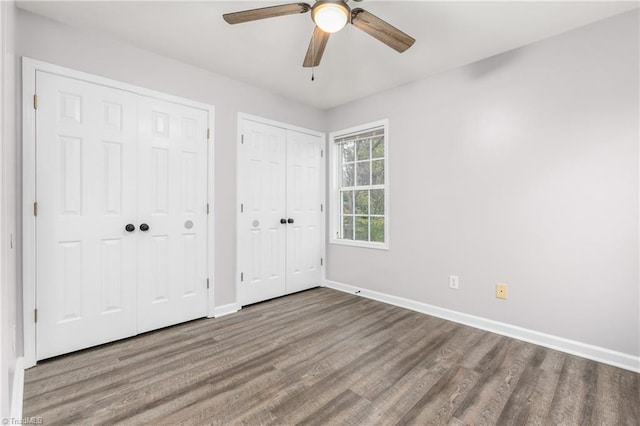 unfurnished bedroom featuring ceiling fan, wood-type flooring, and two closets