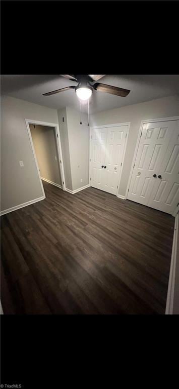 unfurnished bedroom with dark hardwood / wood-style flooring, two closets, and ceiling fan