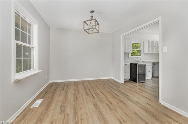 unfurnished dining area with light hardwood / wood-style flooring, beverage cooler, and an inviting chandelier