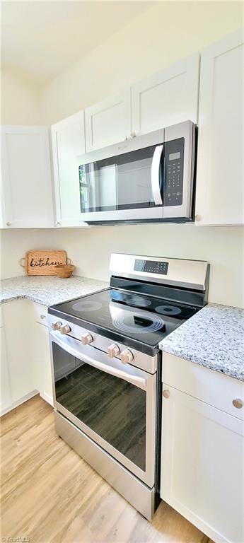 kitchen with appliances with stainless steel finishes, white cabinetry, light wood finished floors, and light stone countertops