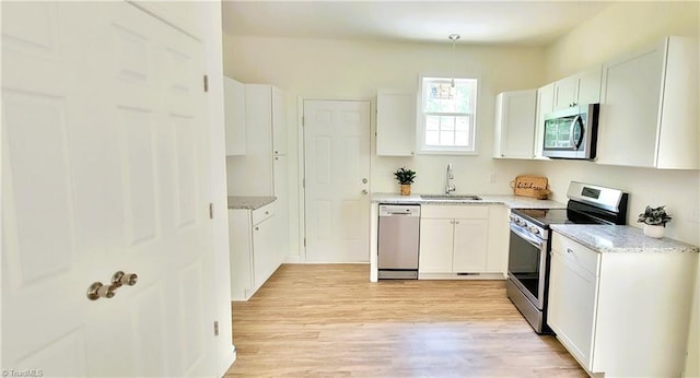 kitchen with appliances with stainless steel finishes, a sink, light wood-style floors, and white cabinetry