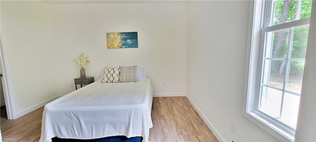 bedroom featuring multiple windows, baseboards, and light wood-style flooring