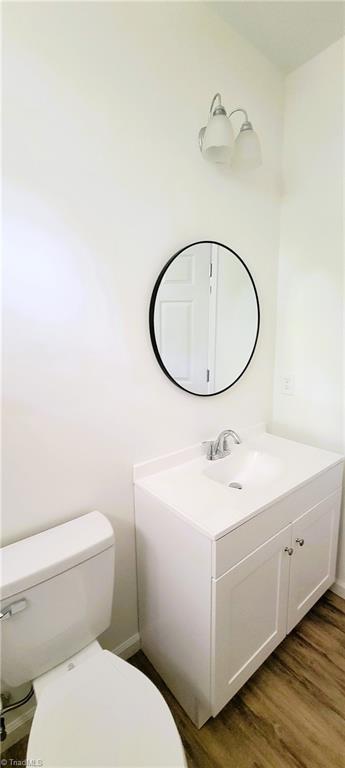 half bath with wood finished floors, toilet, and vanity