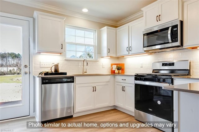 kitchen with appliances with stainless steel finishes, light wood-type flooring, a sink, white cabinets, and ornamental molding