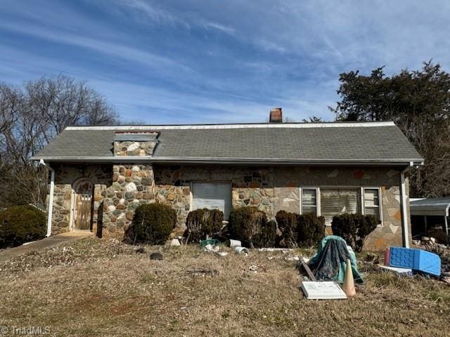 back of property with a shingled roof, stone siding, and a chimney