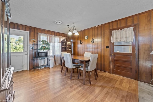 dining area with a chandelier, light wood-type flooring, a textured ceiling, and wooden walls