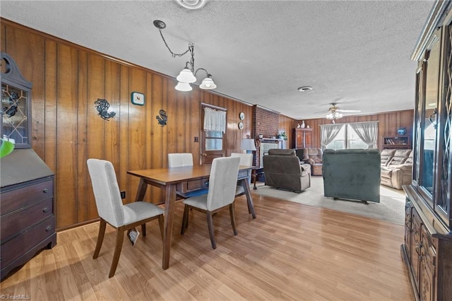 dining area featuring light wood-style flooring, wooden walls, a textured ceiling, and ceiling fan with notable chandelier